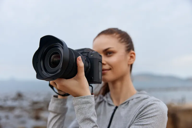 Young female photographer in casual athletic wear capturing nature with a camera, showcasing focus and passion, surrounded by a serene outdoor backdrop