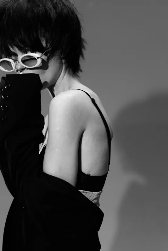 Black and white portrait of a stylish young woman wearing sunglasses and a dark jacket with an elegant, mysterious mood.