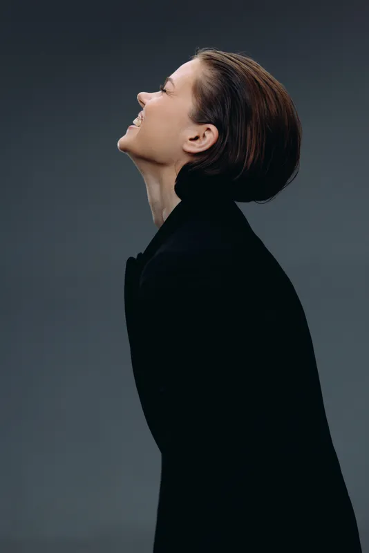 Profile of smiling woman in black coat with short hair against gray background