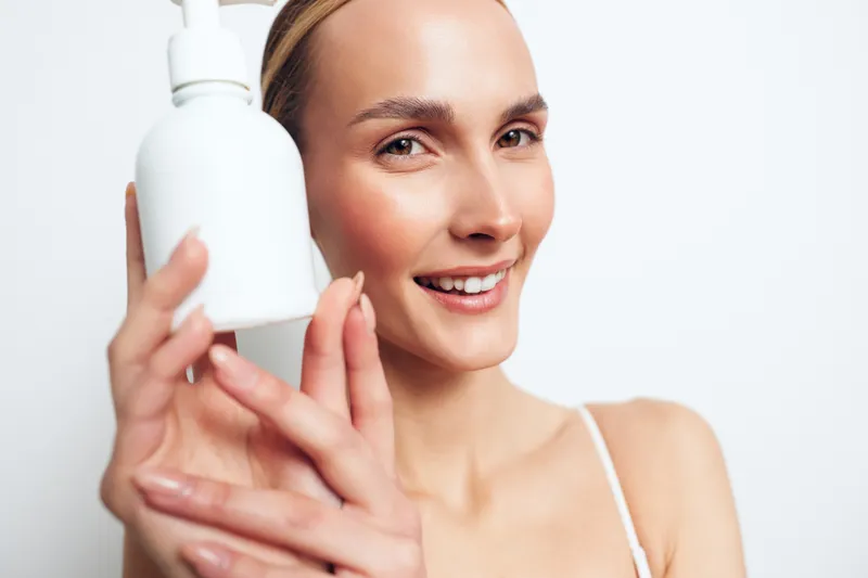 Smiling woman holding white cosmetic bottle, skincare concept, clean skin, natural makeup, bright background, beauty routine, wellness, healthy lifestyle, closeup portrait