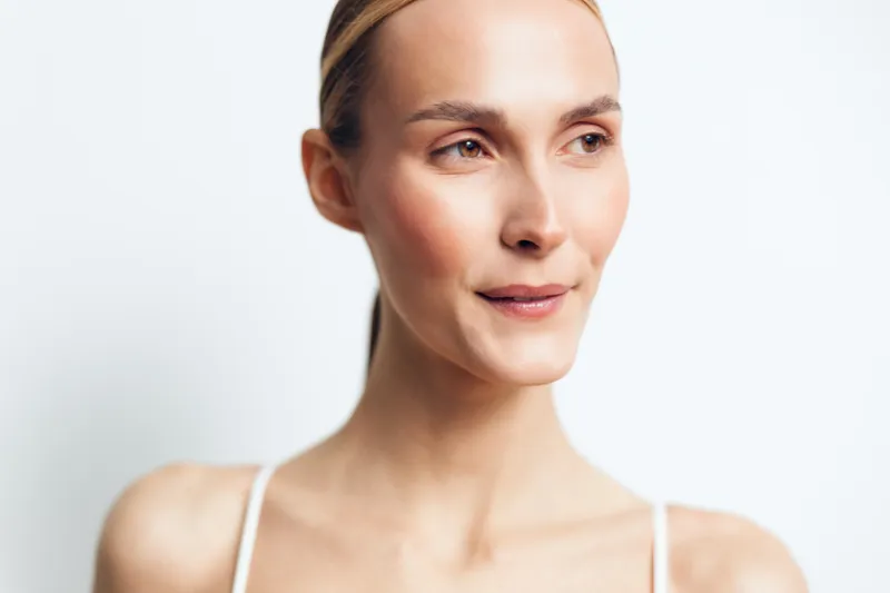 A serene woman with clear skin and natural makeup looks away thoughtfully against a white background. Concept for beauty, skincare, health, and calm expression.
