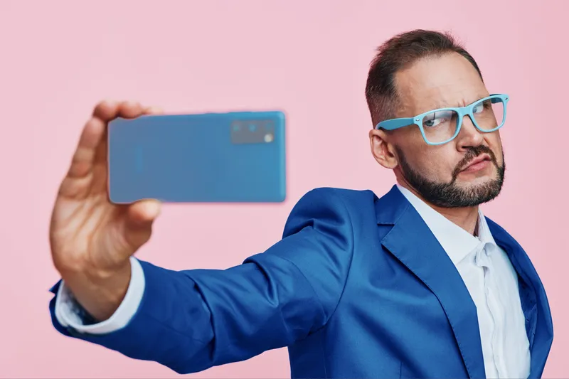 A professional man in a blue suit poses confidently with a smartphone against an isolated pink background, conveying modern business energy, focus, and a dynamic mood.