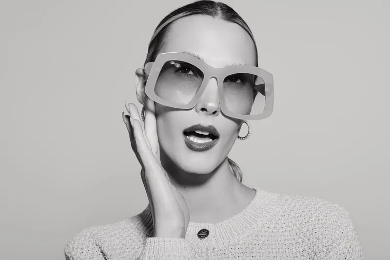 Portrait of a white caucasian woman with fair skin wearing oversized sunglasses and a knitted sweater. Fashion concept with retro style and confident expression on neutral background.