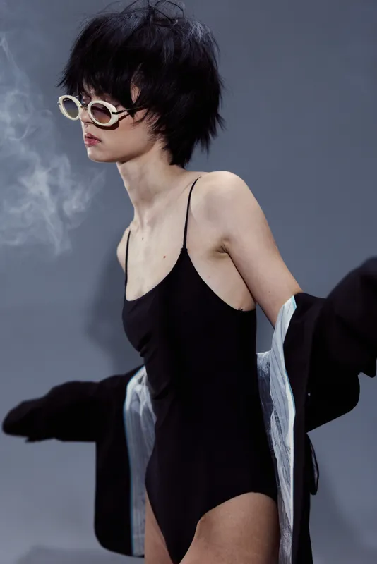 Young woman wearing black swimsuit and stylish sunglasses posing with confident attitude and short hair in cool atmosphere.