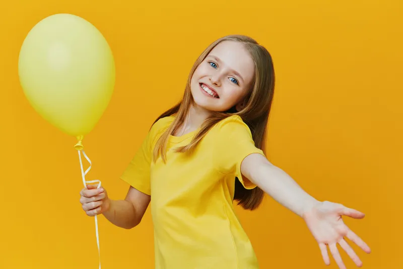Happy girl in a yellow t shirt holding a balloon, set against a vibrant yellow background, conveying joy and celebration in a cheerful atmosphere