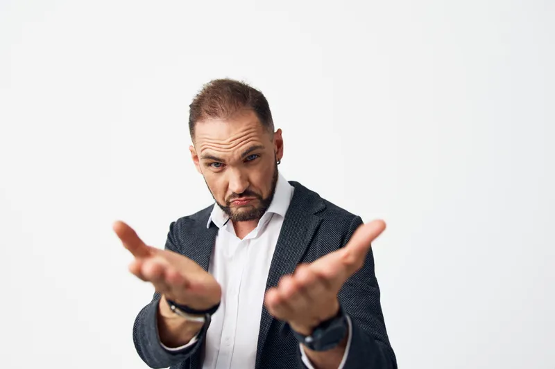 A focused business professional man stands against a vibrant colored isolated backdrop, presenting with open hands to convey invitation, concern, and clear guidance for clients.