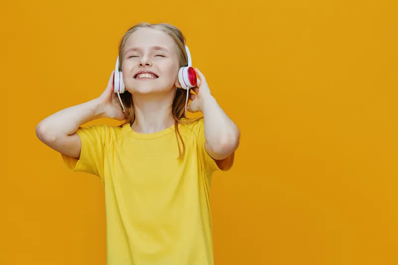 Happy girl with headphones enjoying music, wearing a yellow t shirt against a bright yellow background, conveying joy and energy