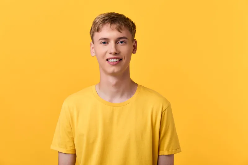 Young man, casual clothing, yellow background, cheerful smile, sunny studio setup showing modern street style and approachable mood, ideal for fashion and lifestyle campaigns