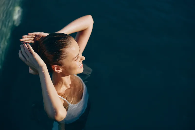 Bright, calm scene of a woman floating in clear water, eyes closed, gentle smile, sunlit reflections on the surface, soft buoyancy, relaxed posture, natural colors, tranquil mood