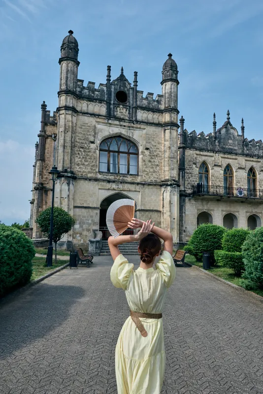 Tourist woman in a pale dress walks toward a grand castle like structure with ornate towers capturing a moment of awe and exploration