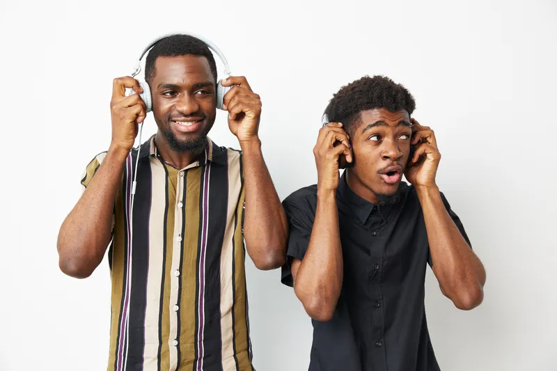 Two black men enjoying music with headphones, showcasing joy and connection. Stylish outfits bring a fresh vibe to this vibrant moment of happiness and friendship.
