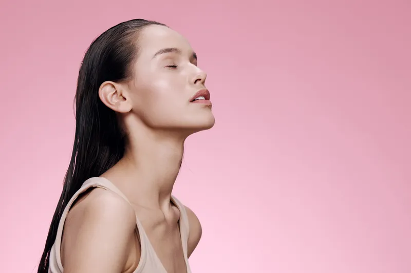 Young woman with smooth skin and wet hair against a soft pink background, showcasing serenity and beauty Focus on skincare, wellness, and natural beauty
