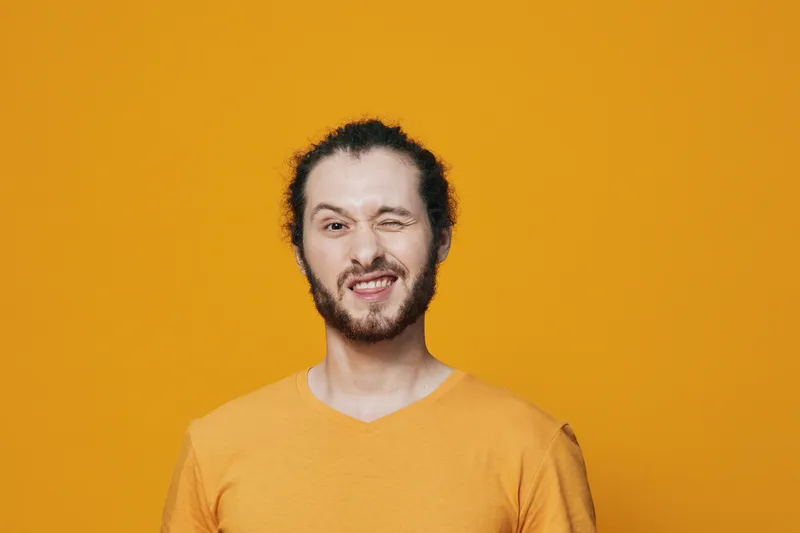 Young man winking on a vibrant orange background, showcasing a playful expression in a casual yellow shirt, perfect for cheerful lifestyle concepts
