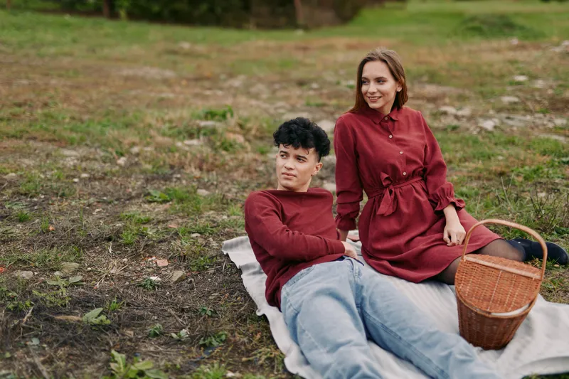 Candid outdoor portrait of a young couple on a picnic blanket, conveying authenticity and credibility through natural poses, casual clothing, warm expressions and relaxed posture.