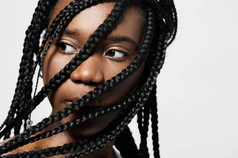 Close up portrait of a young Black woman with braided hair, showcasing her thoughtful expression against a clean white background