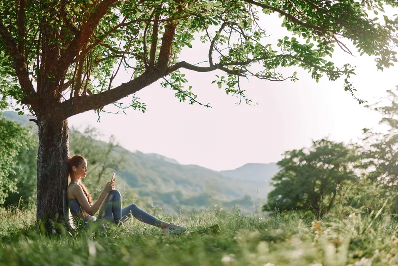 Young woman enjoying a peaceful moment under a tree in a lush green field, representing tranquility and connection with nature in a spring setting