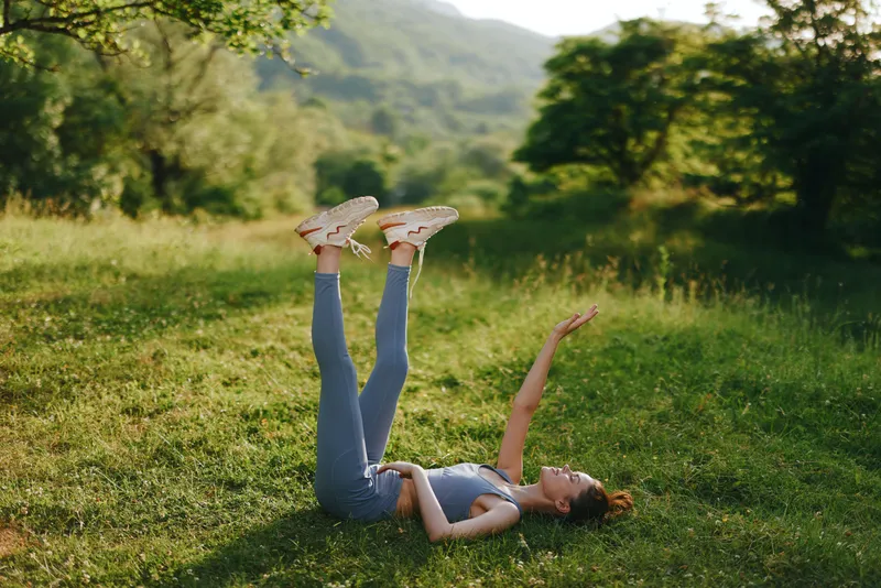 A young woman doing yoga outdoors with legs raised in a lush green meadow, expressing tranquility and relaxation in nature Exercise, outdoor yoga, peaceful moment