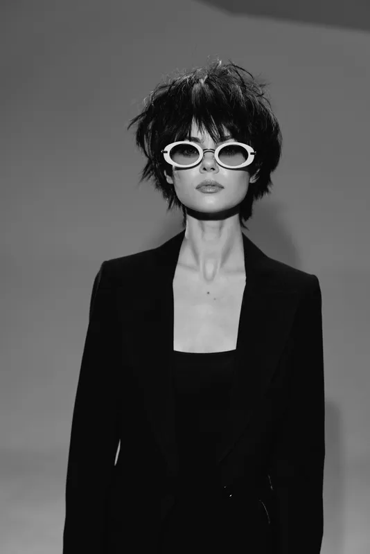 Stylish woman with sunglasses in black and white wearing a suit with a confident expression and tousled hair.