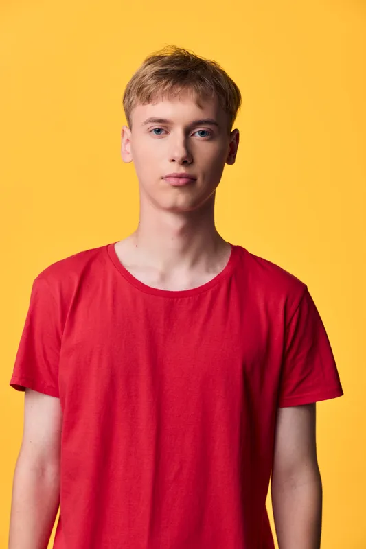 Man wearing a red t shirt stands against a bright yellow backdrop, clean studio lighting and minimal setup, casual fashion vibe with bold color and relaxed stance for a fresh stock shot.