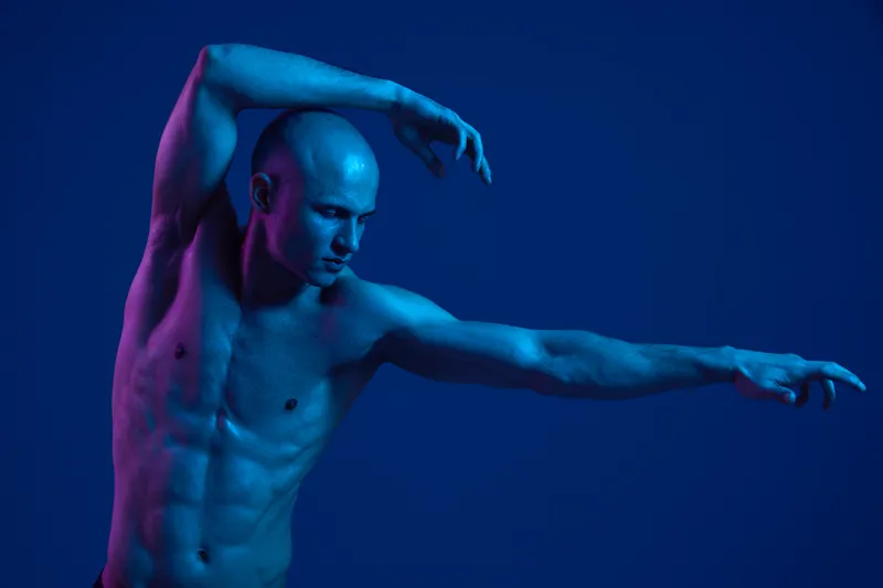 Athletic man posing in dynamic movement, showcasing strength and grace with vibrant blue lighting creating a captivating atmosphere.