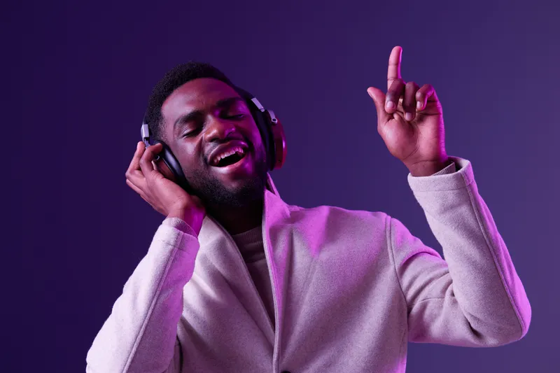 Young man enjoying music with headphones, expressing joy in a purple lit environment, conveying a sense of happiness and relaxation