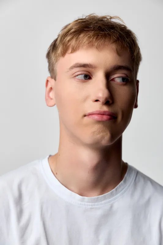 Young man in a white shirt with a thoughtful expression, studio lighting, looking away from the camera, conveying casual style, introspection, and calm mood.