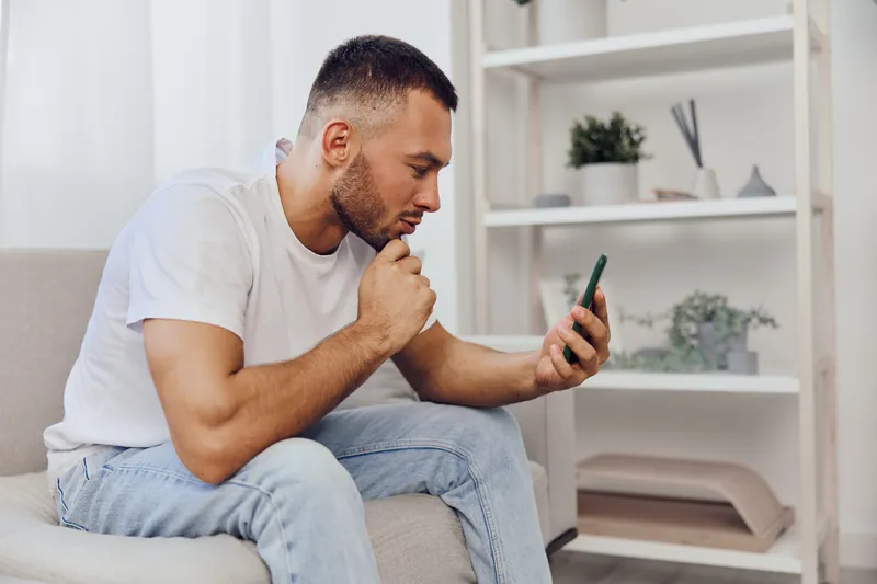 Thoughtful man browsing on smartphone, dressed casually, showing focused expression, surrounded by modern interior decor. Inspired by minimalist trends in lifestyle.