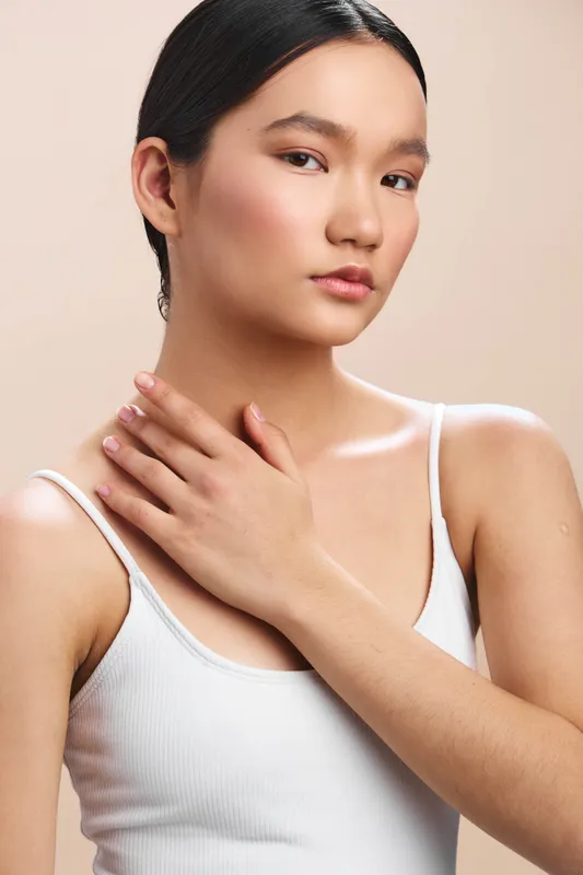 Asian woman gazes softly at the camera in a clean studio, conveying elegance and confidence. The calm expression and smooth skin create a refined, professional portrait tone.