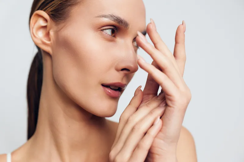 Woman, face, skincare, beauty, hand, touching, closeup, portrait, studio, softlight, young female applying moisturizer, calm expression, fingertips on cheek, clean white background, natural glow