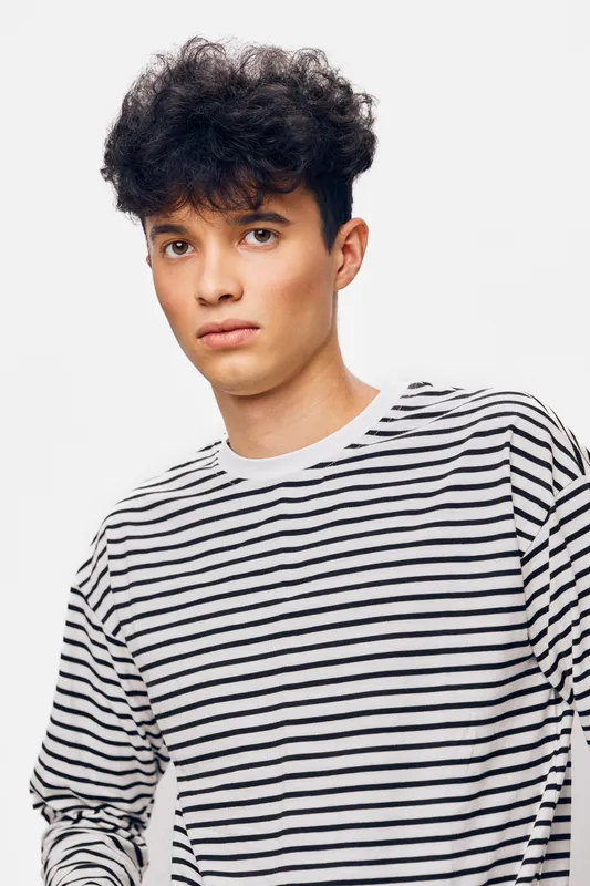 young man with curly hair wearing striped shirt, looking calm and thoughtful against a white background, casual modern style portrait with neutral expression