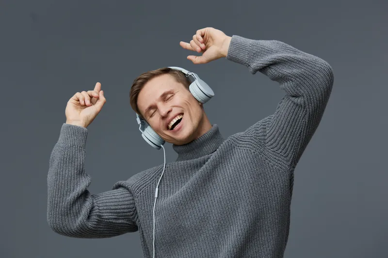 happy young man listen music wear grey knitted sweater headphones enjoy sound with closed eyes isolated on grey background digital detox concept