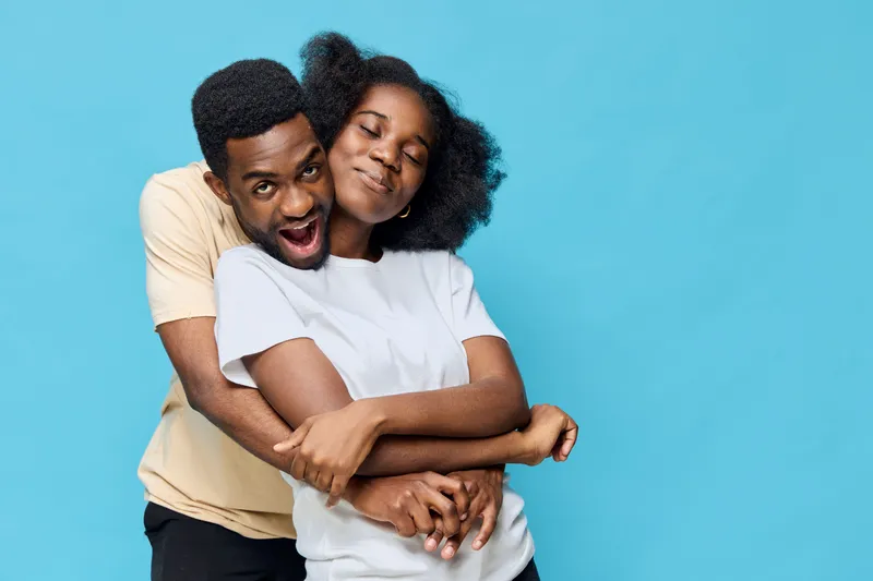 Happy African couple embracing each other with joy, wearing casual clothes, against a vibrant blue background, symbolizing love and unity