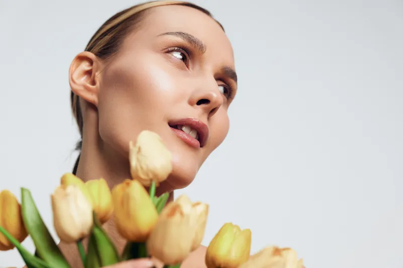 Portrait of a smiling woman holding a bouquet of tulips, bright yellow petals, soft light, warm tones, isolated on a light backdrop, conveying freshness and elegance