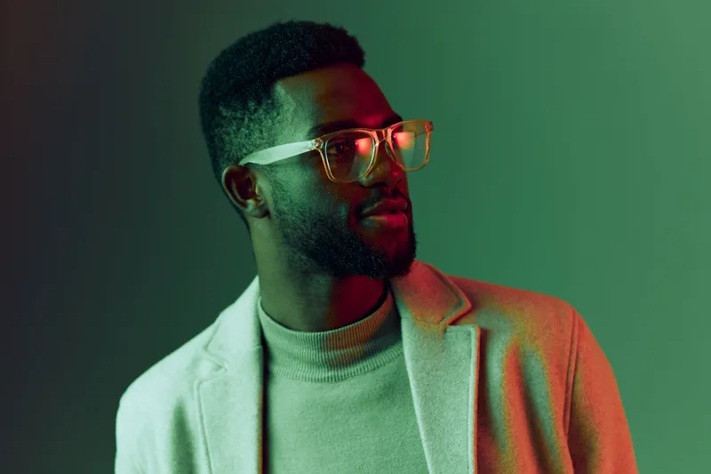 Stylish African man in glasses wearing a fashionable outfit, exuding confidence and elegance against a vibrant green and red background