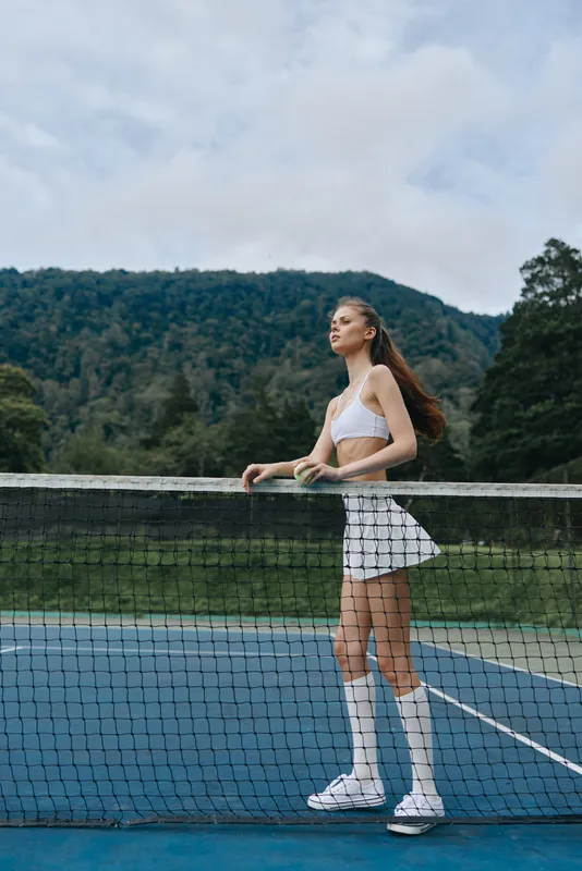 Young athletic woman in a white outfit on a tennis court, showcasing confidence and joy in a scenic outdoor setting