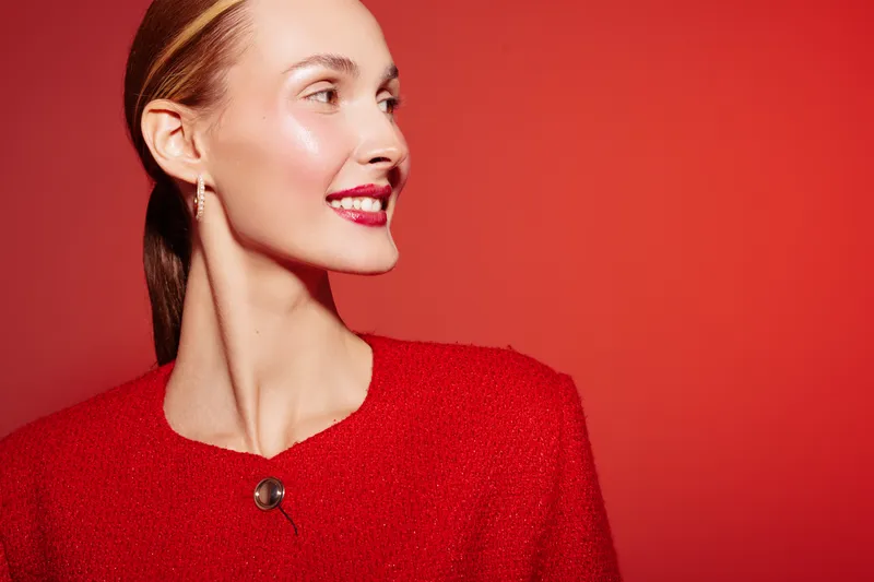 Portrait of a smiling woman with slicked hair wearing a red textured sweater against a red background. Concept of fashion, beauty, confidence, and vibrant style in studio lighting.