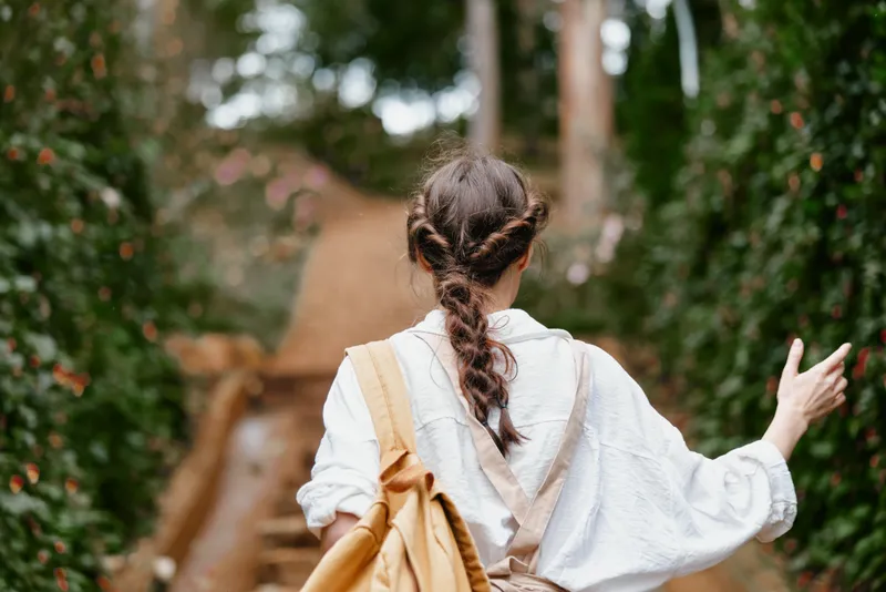 Young woman walking through a lush garden, wearing a white shirt and brown overalls, conveying a sense of peace and connection with nature