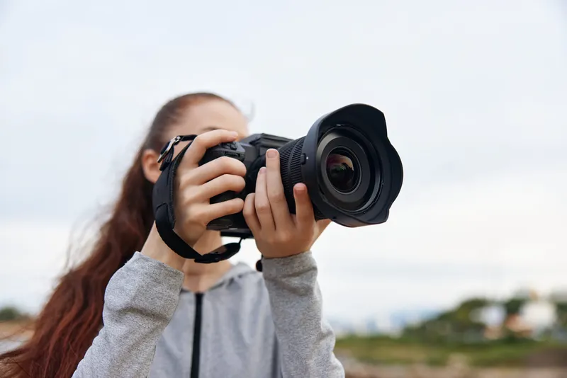 Young woman with long hair taking photos with a professional camera in a casual outfit, capturing natural moments in the great outdoors