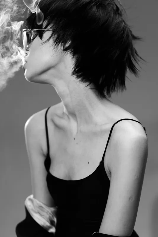 Black and white portrait of a woman smoking with a contemplative expression in a minimalist style.