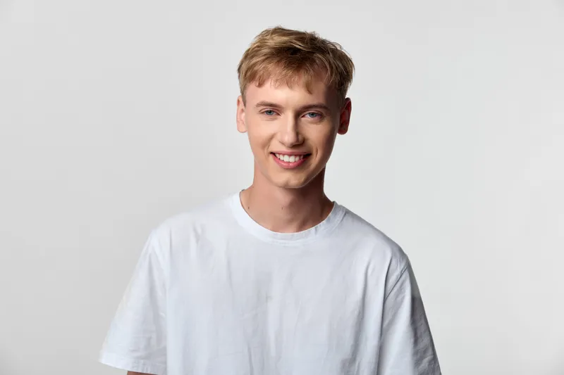 Smiling man in a white t shirt in a bright studio, casual pose, clean backdrop, friendly and approachable vibe, everyday fashion and relaxed mood