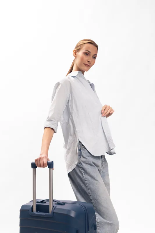 Young woman in casual clothing stands with suitcase on white background, ready for travel. Concept for vacation, journey, and lifestyle with confident expression.