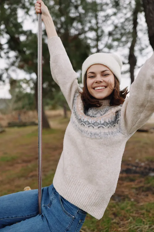Woman on a swing in an outdoor park, wearing a cozy sweater and beanie, joyful smile, candid moment, casual autumn mood, fresh air and carefree energy.