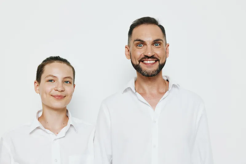 Business professional man with a confident, calm smile stands beside a colleague against a clean white background, conveying focus, approachability, and positive energy.