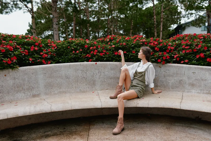 Young woman in casual summer outfit sitting on stone bench surrounded by vibrant flowers, expressing relaxation and serenity in a natural setting