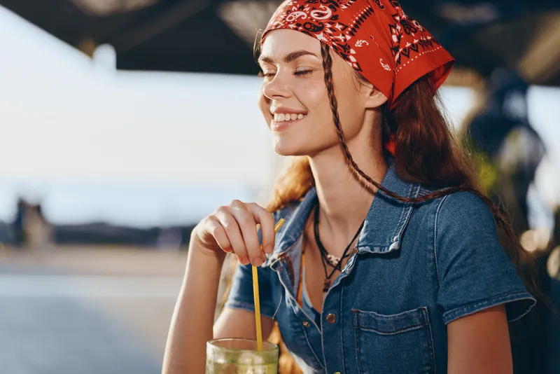 lifestyle woman in modern boho-western denim street style smiling with drink outdoors, film color tones creating relaxed summer vibe