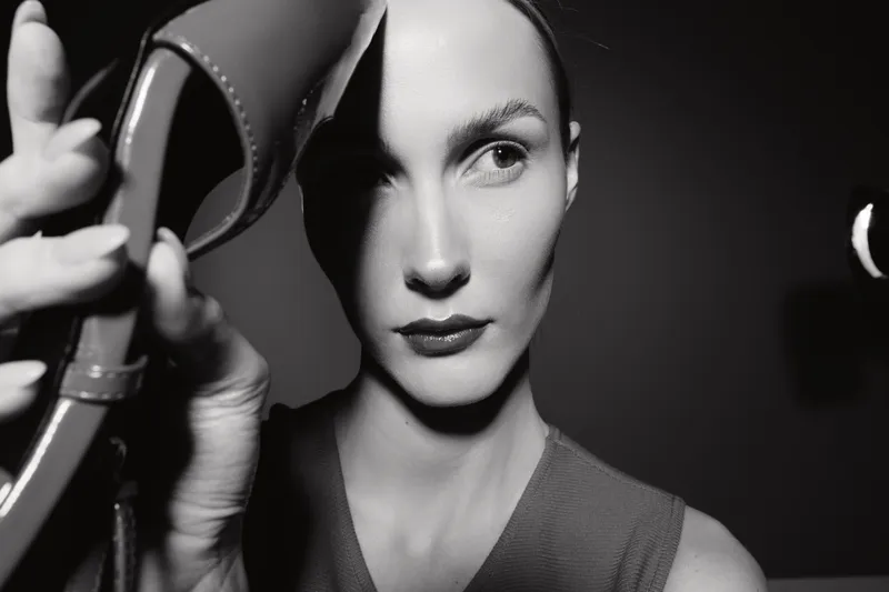 Close-up portrait of a fair-skinned Caucasian woman holding a high heel shoe near her face in dramatic black and white lighting. Concept of fashion, style, and elegance.