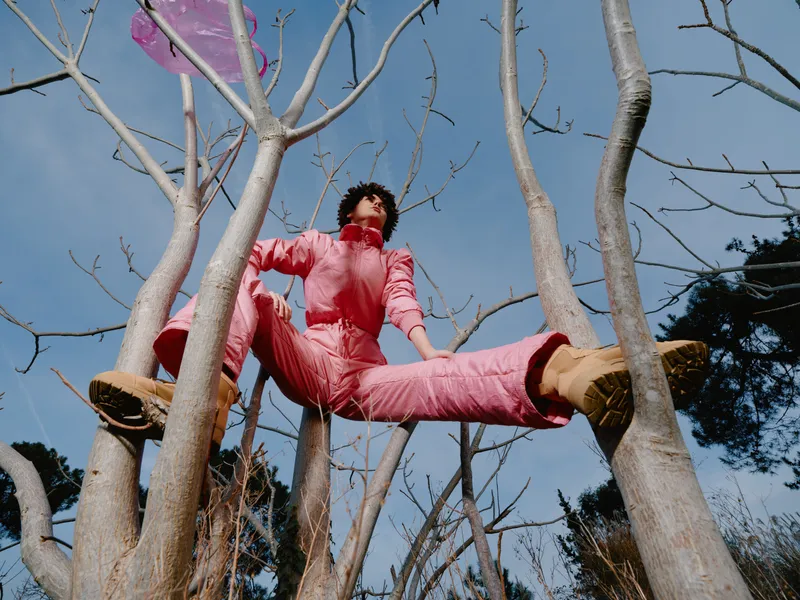 Outdoors adventure, tree climbing with a person in pink outfit, jumping between branches against a clear blue sky, energetic pose and playful mood captured from a low angle.