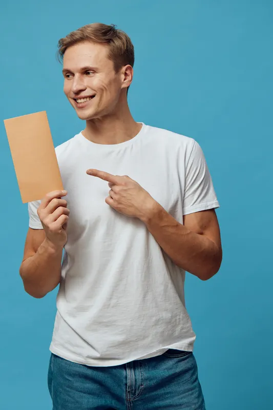 smiling man pointing blank card wear white tshirt casual look isolated blue background communication digital nomad concept