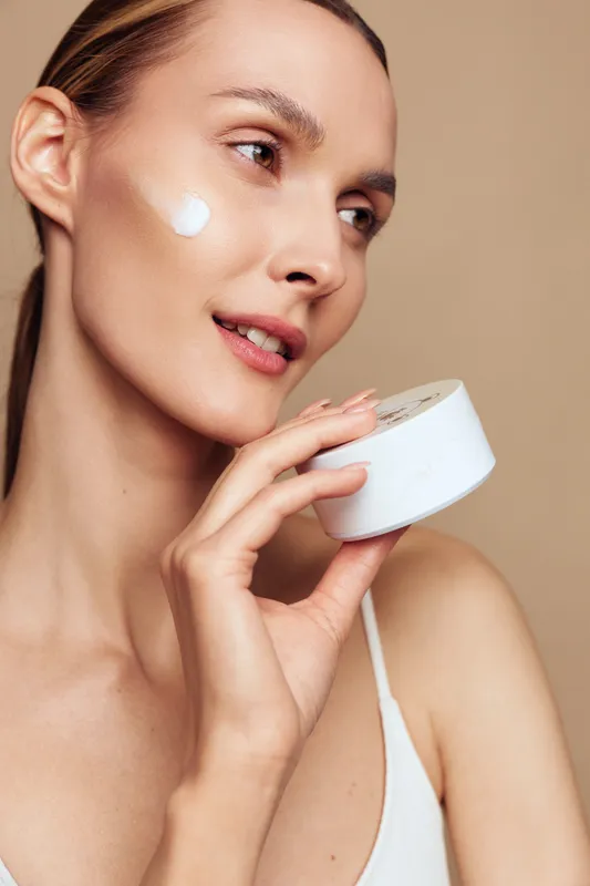 Woman applying white cream on her face, closeup portrait on beige background, skincare and beauty concept, soft studio lighting, calm wellness, self care, spa mood