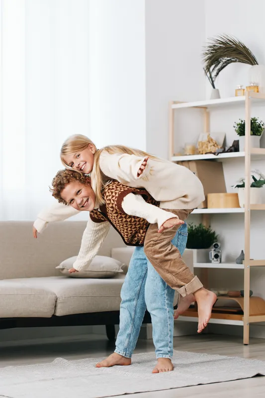 Main focus depicts a man giving a joyful piggyback ride to a child indoors, capturing candid family fun, bonding, and carefree moment.